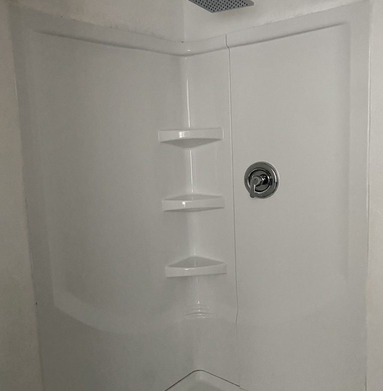 A corner shower with white walls and a black handle.