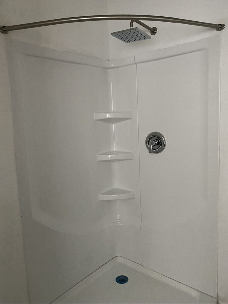 A corner shower with white walls and a black handle.