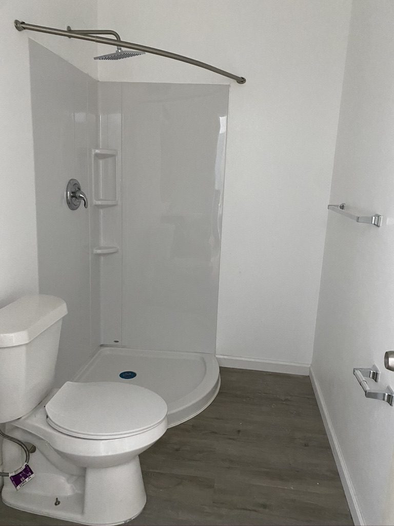 A bathroom with a toilet, shower and wood flooring.