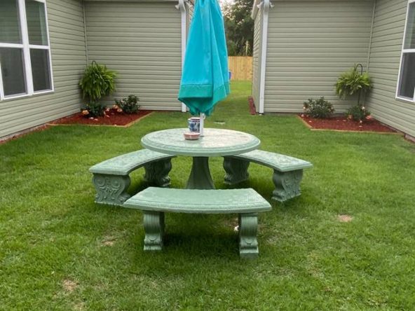 A green table and bench set in the middle of an enclosed yard.