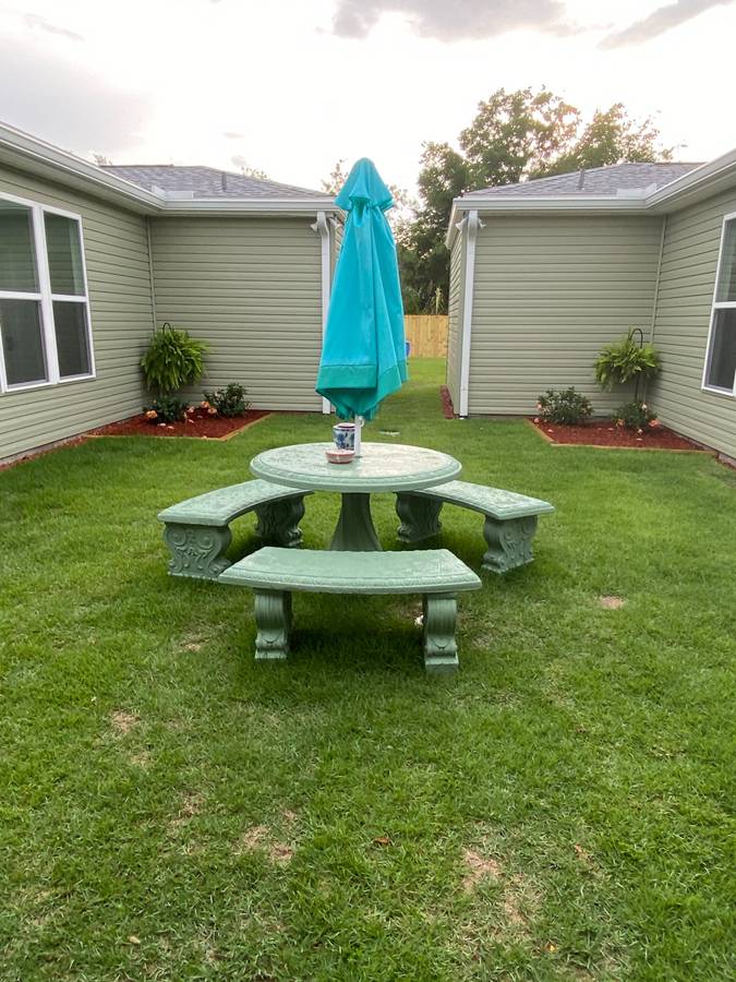 A green table and bench set in the middle of an enclosed yard.