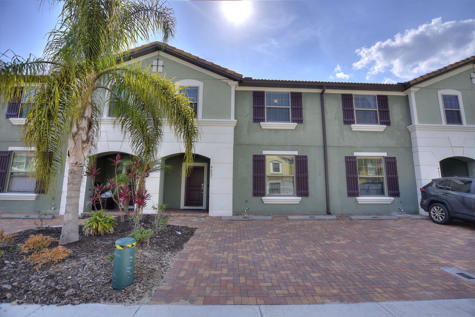 A large house with a brick driveway and palm tree.