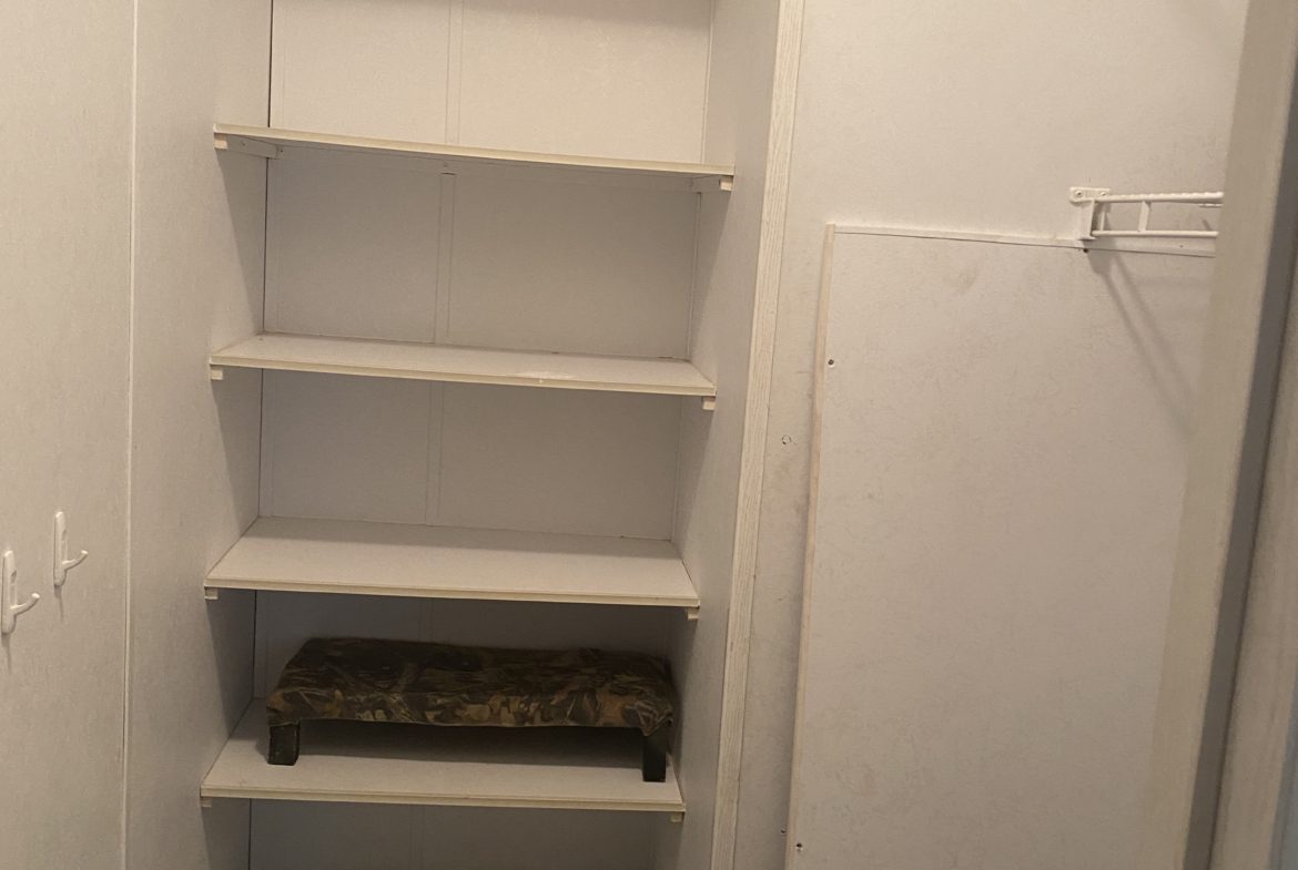 White shelves in a closet with a stool.