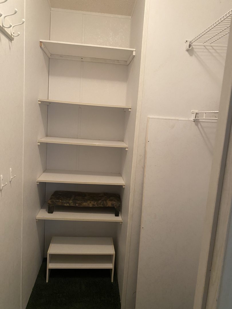 White shelves in a closet with a stool.